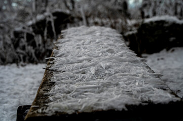 Frost fallen from the trees on a wooden bench in the winter forest, creating a cold and quiet scene.