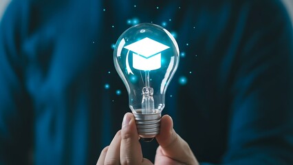 Close-up of a hand holding a glass light bulb with a white graduation cap silhouette, symbolizing education, ideas and innovation