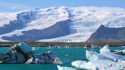 Massive glacier meets a glacial lagoon with floating blue icebergs under a blue sky © HABI ANGGARA PUTRA