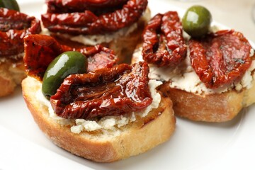 Delicious bruschettas with cream cheese, sun-dried tomatoes and green olives on plate, closeup