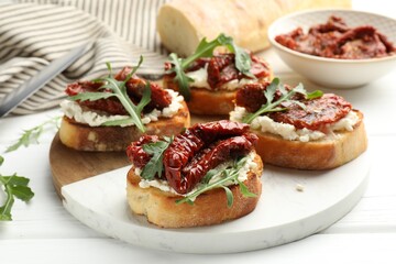 Delicious bruschettas with cream cheese, sun-dried tomatoes and arugula on white wooden table, closeup