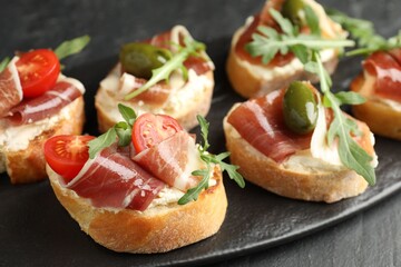 Delicious bruschettas with cream cheese, prosciutto, green olives, tomatoes and arugula on table, closeup