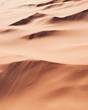 Wavy desert sand dunes with warm orange and light brown tones, showcasing natural textures and abstract patterns created by wind and light, a serene arid landscape photo.