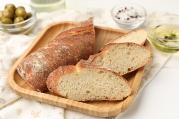 Slices of baguette with oil and olives on white wooden table, closeup