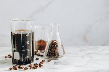 Laboratory glassware with tasty coffee, beans and powder on white marble table, closeup. Space for text