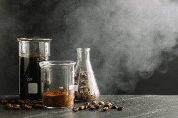 Laboratory glassware with tasty coffee, beans, powder and smoke on black table, space for text