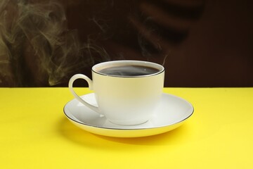 Obraz premium Aromatic coffee in cup on yellow table against dark background