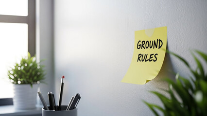 Yellow sticky note with ground rules on office wall near window
