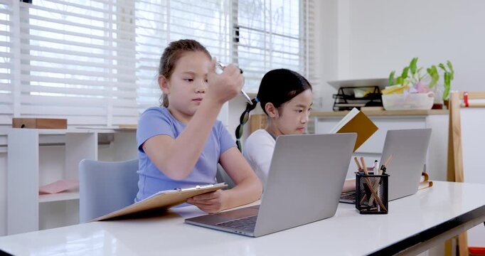 Two preteen girls asian and caucasian working with laptops during classroom slowmotion digital learning activity representing collaboration teamwork education childhood study communication