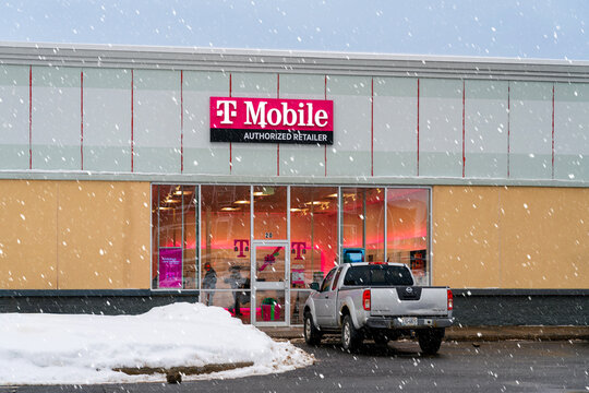 Rome, NY - Dec 17, 2025: T-Mobile Authorized Retailer storefront during active snowfall, with magenta signage, glass facade, and parked pickup truck outside a brightly lit wireless retail location
