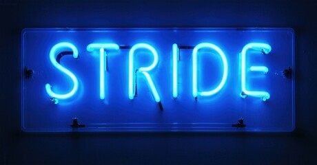 Bright blue neon sign spells STRIDE. Rectangular frame, dark background. Simple design, modern aesthetic. Illuminated letters stand out.