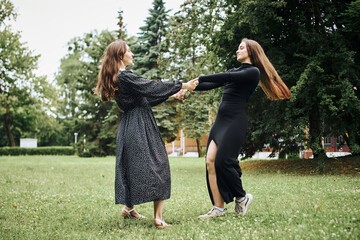 Two young women holding hands and spinning in grassy park