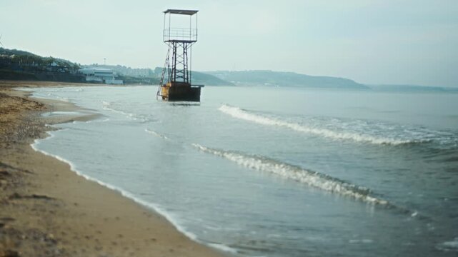 Peaceful seaside scene showing gentle waves rolling onto an empty beach with a lifeguard tower, evoking solitude and coastal calm.  
