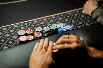 Casino poker table detail showing player hands protecting cards beside stacked betting chips, highlighting wagering behavior and risk management in live gaming