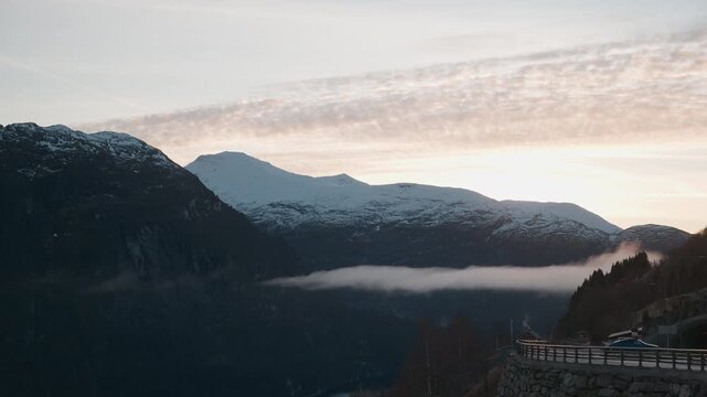 Scenic shot from Lj&oslash;en view point towards Hellesylt, with snow covering the mountains and a sunset in the background