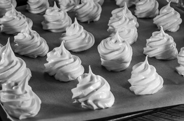 Beautiful shiny meringues on a baking tray in rows, lots of them