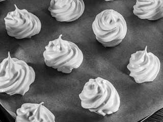Top view of meringues made from egg whites and sugar, piped onto baking paper with a pastry tip
