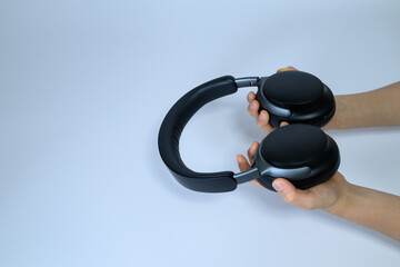 Person hands holding a pair of black wireless headphones over white background