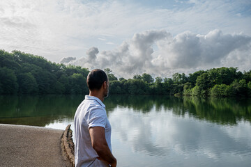 A man stands on a beach looking out at a lake. The sky is cloudy and the water is calm