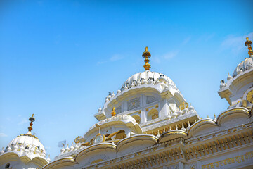 Nanded, MH, India, Dec 21, 2025: View through a metal gate framing the saffron Nishan Sahib flag pole and golden dome of Hazur Sahib Gurudwara with a flying bird.