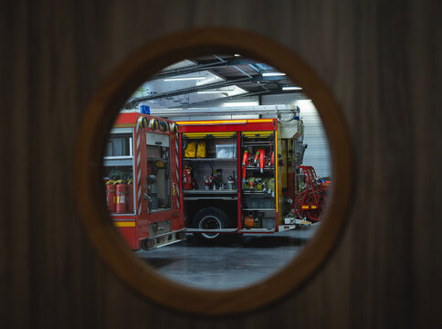 Vue &agrave; travers un hublot de camions de pompiers rouges stationn&eacute;s dans un garage de caserne avec &eacute;quipement de secours