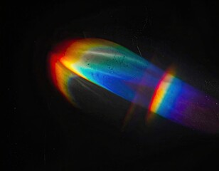 A spectrum of refracted light streaks across a dark, grainy surface