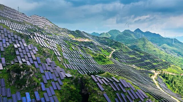 Aerial shot of large solar power station on green mountain slopes 