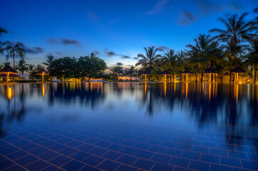 Tranquil resort swimming pool in Mauritius with palm trees and lights after sunset.