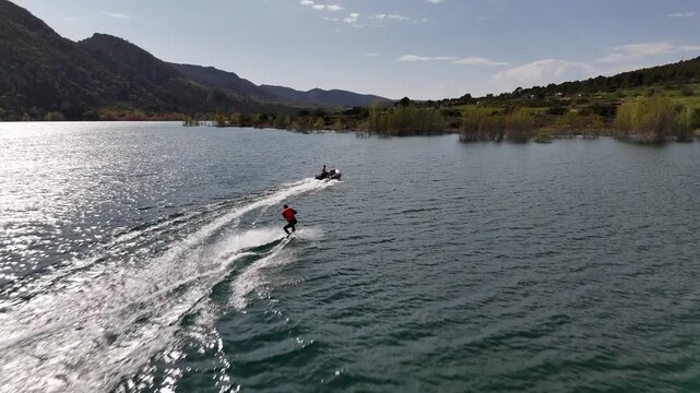 Wide shot of wakesurfing behind a boat on a calm mountain lake. Scenic landscape, lifestyle, summer recreation and outdoor freedom.