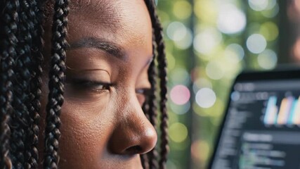 Focused African American female software engineer with braided hair intently coding on a laptop screen - Powered by Adobe
