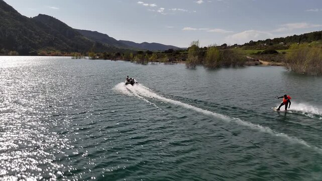Wide shot of wakesurfing behind a boat on a calm mountain lake. Scenic landscape, lifestyle, summer recreation and outdoor freedom.
