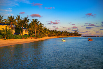 Peaceful beach scene at sunset in Bel Ombre, Mauritius, with palm trees, boats, and coastal hotels and resorts.