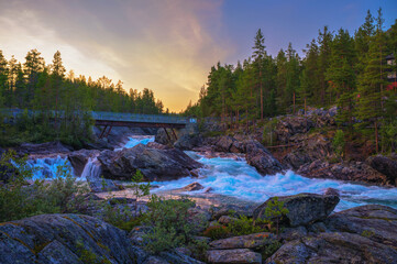 Sunset view of Pollfoss waterfall on the Framruste River near Billingdalen in Oppland, Norway, surrounded by forest and rocky terrain.