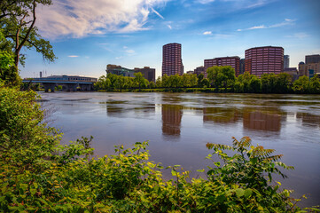 View of Hartford, Connecticut downtown skyline with modern office buildings, Founders Bridge, and reflections on the Connecticut River framed by greenery
