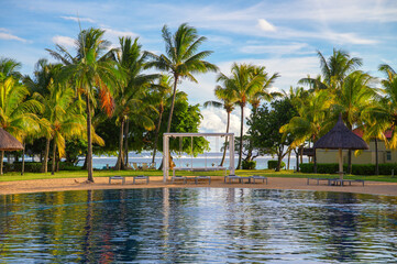 Scenic view of a tropical resort pool with lounge chairs, palm trees, and beach access in Mauritius.