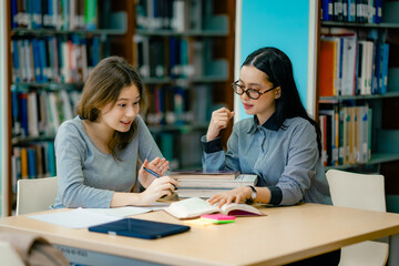 Tutor teaching student during study session at library desk with open textbook sharing knowledge mentoring education progress.