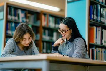 Two women reading research materials together at library table with open academic books analyzing information scholarly study environment.