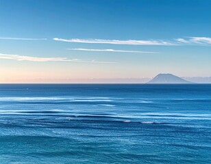Obraz premium Distant island rises from a serene ocean under a clear blue sky