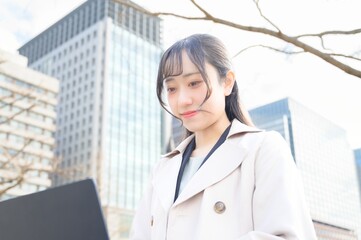 オフィス街でノートパソコンを持つビジネスウーマン
