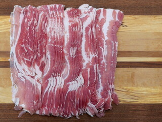 Smoked, thinly sliced ​​bacon with its visible fat structure is stacked on a wooden board. Top view. Copyspace.