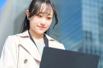 オフィス街でノートパソコンを持つビジネスウーマン