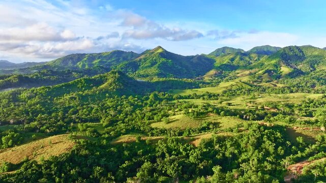A landscape of mountain peaks against a cloudy sky. A mountain valley in the rays of the morning sun. The vibrant tropical nature of the Dominican Republic. Multicolored hills with green meadow grass.