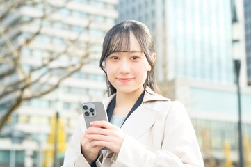 オフィス街でスマホを使用する20代のビジネスウーマン