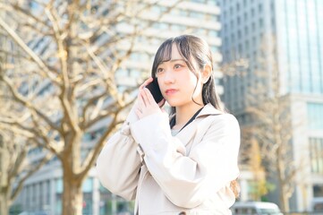 オフィス街でスマホを使用する20代のビジネスウーマン
