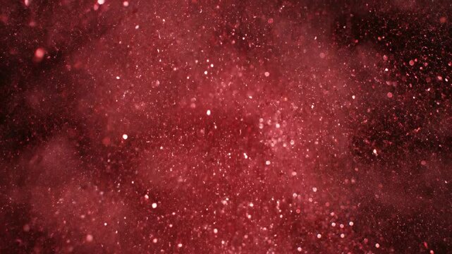 Extreme close-up slow motion shot of fine ruby red glitter dust exploding outward and slowly dissipating against a solid black backdrop providing isolated texture burst, macro, graphic