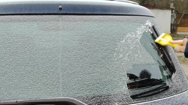 Zdrapywanie szronu z przedniej szyby samochodu skrobaczką &ndash; zimowy poranek, przygotowanie auta do jazdy.