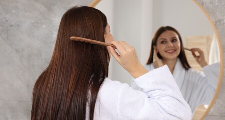 Fototapeta premium Woman in bathrobe brushing her hair near mirror indoors, selective focus
