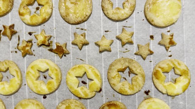 Freshly baked Alsatian bredele butter cookies in star and ring shapes on parchment-lined baking tray, golden brown with egg-wash glaze for Christmas holiday treats