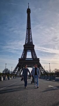 A romantic parisian moment with a couple walking handheld towards camera with the majestic Eiffel Tower centered behind them. Graceful lovers share a sweet kiss, perfectly framing their love