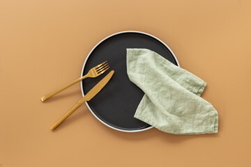 Top view of minimalistic table setting with empty plate, cutlery and napkin on brown background,...
